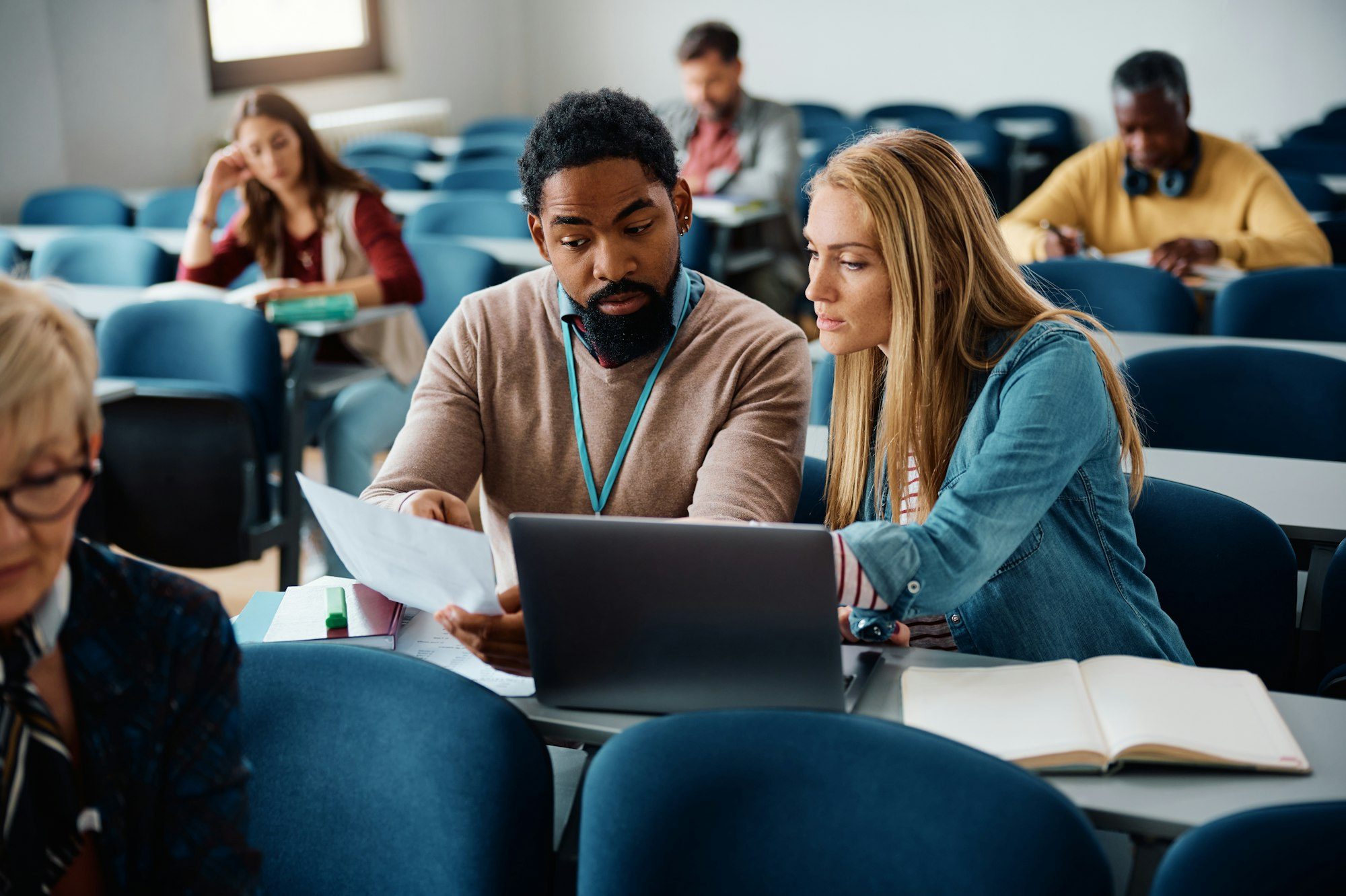 Black adult education teacher assisting his student with assignment during a class in the classroom.